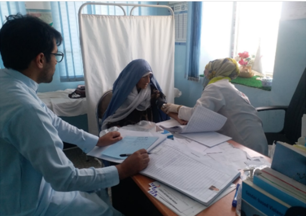 health worker provides care to patient another heath worker sat at a desk looking on